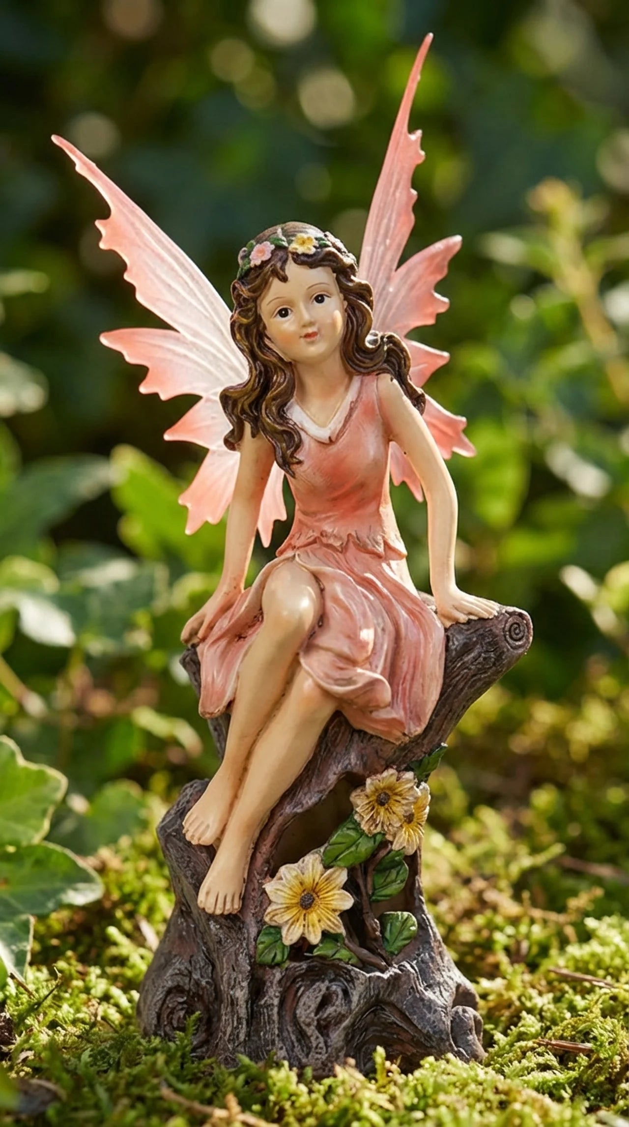 Garden fairy figurine with pink wings and dress sitting on a branch with flowers.