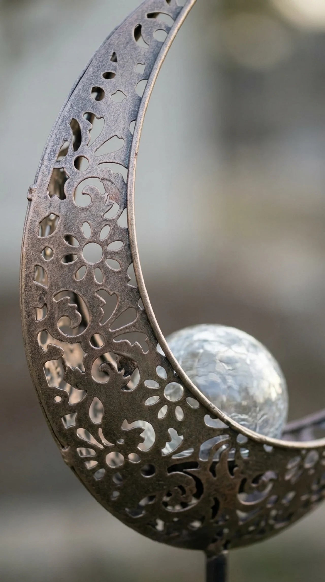 Close-up of filigree cut floral scroll pattern on iron crescent moon solar garden stake 